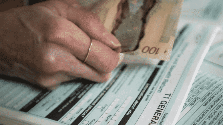 person filling out T1 tax form holding Canadian money