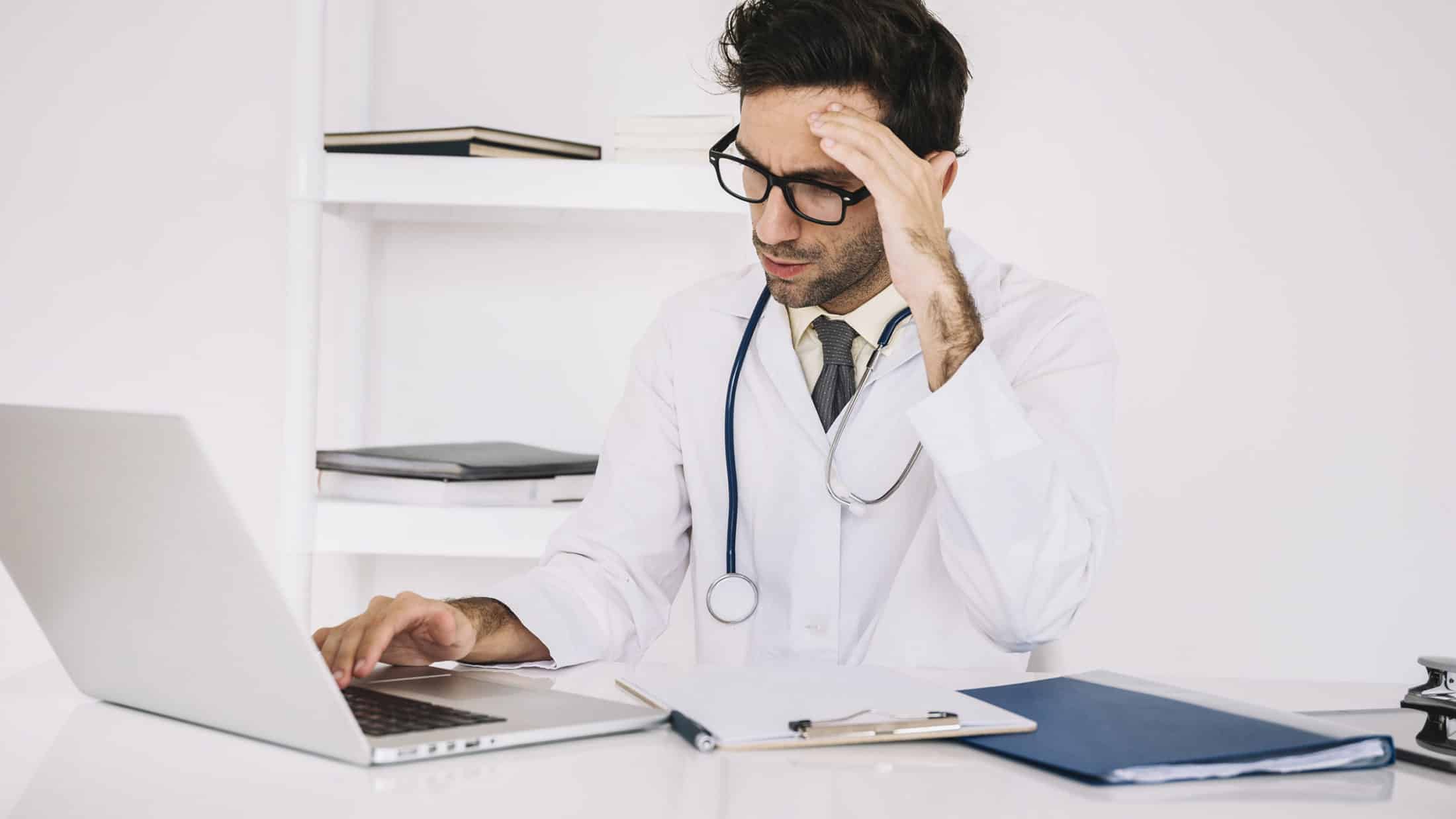 tired male doctor working on a laptop in a clinic